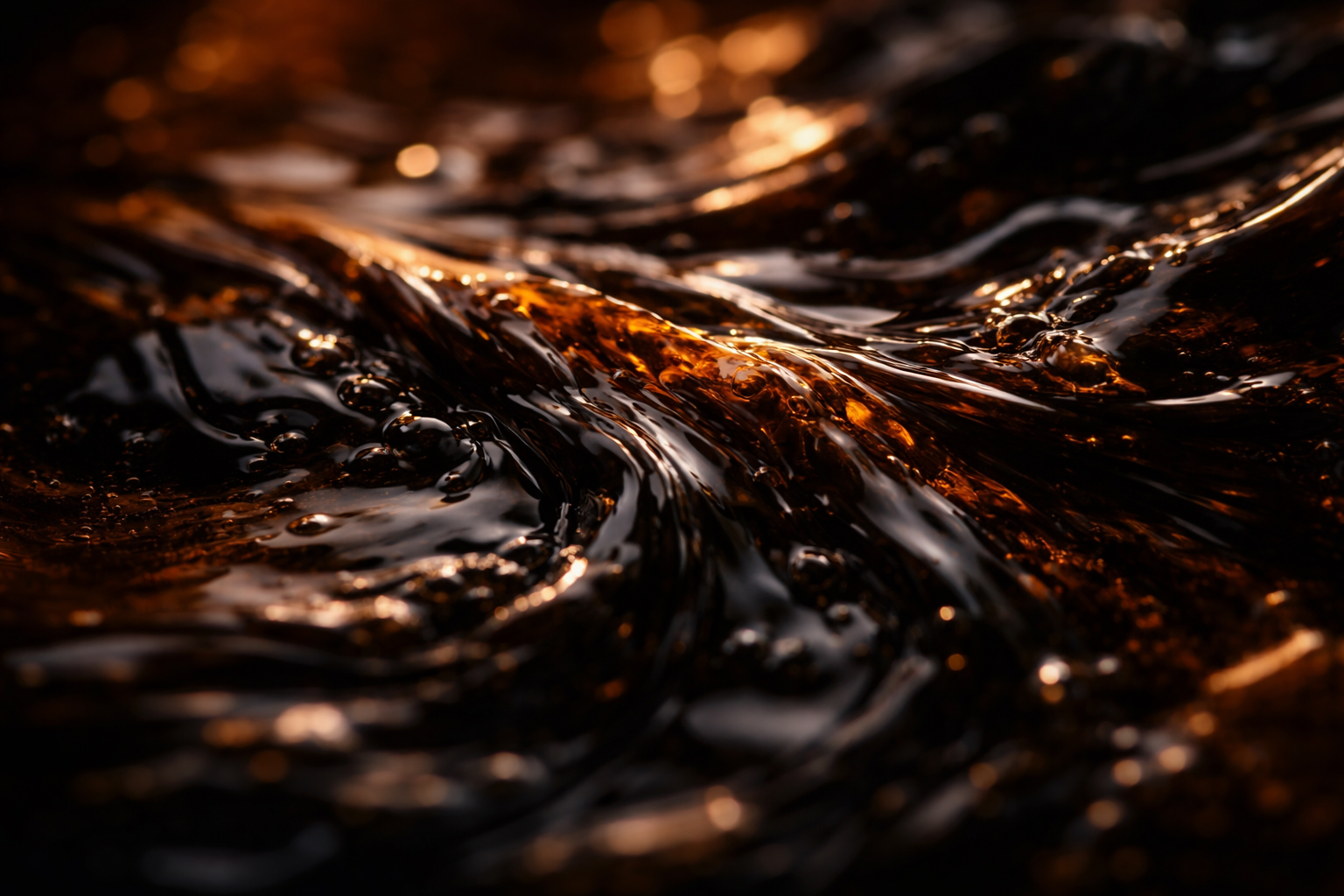 A close-up macro photograph of crude oil with light playing across its viscous amber-brown surface, shot from an angled overhead perspective.