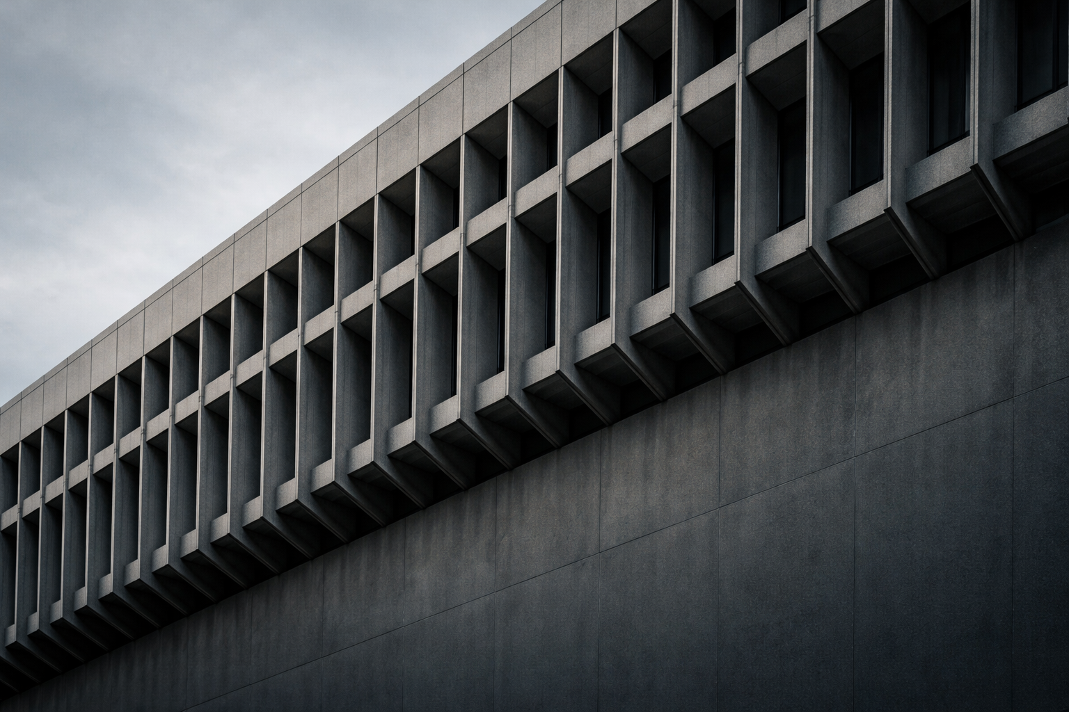 Dark silhouetted concrete sunshade fins rise across the upper part of a muted blue-grey sky above a plain shadowed wall.