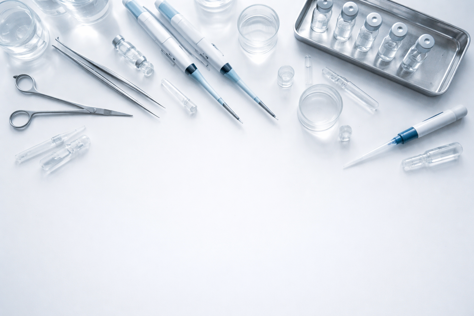 An overhead view of glass laboratory vials and medical instruments neatly arranged on a white surface with soft natural lighting.