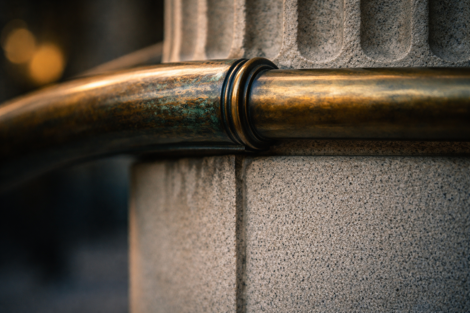 Tight macro of a fluted limestone column meeting a weathered bronze handrail, warm highlights and cool stone tones with a soft, out-of-focus background and an empty lower third.
