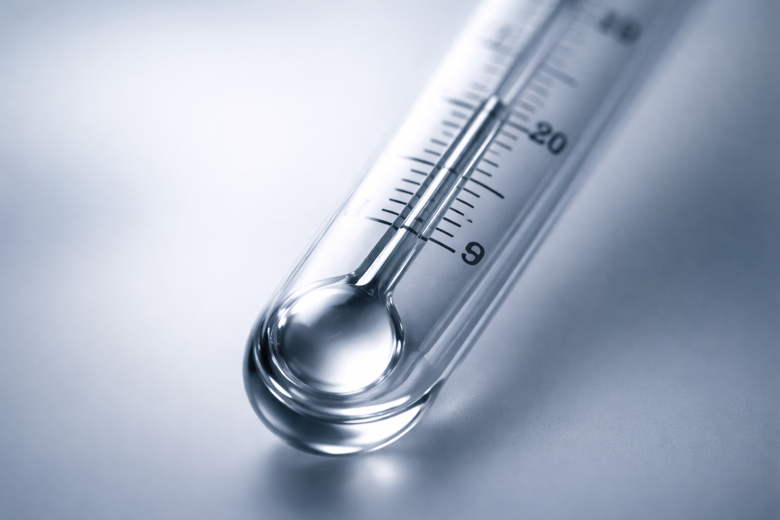 A thermometer's mercury column rises through measurement markings, photographed in soft backlight with selective focus on the graduated scale.