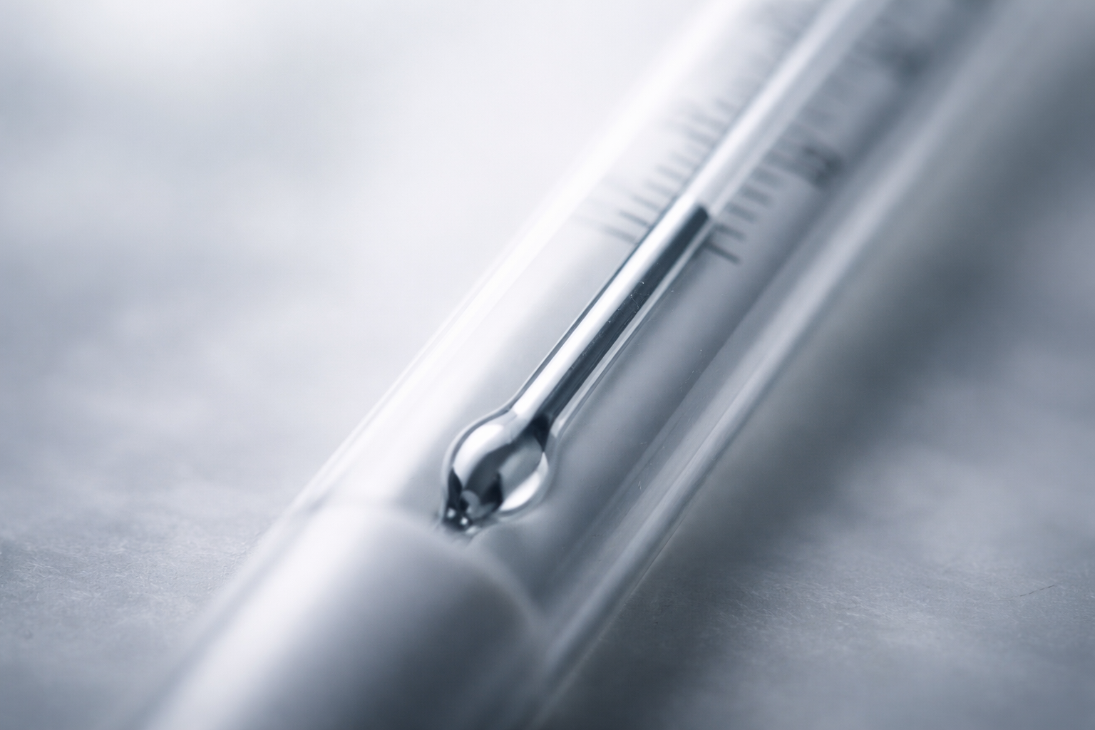 A close-up of a mercury thermometer with the liquid level rising, photographed with soft natural light and shallow focus, suggesting measurement and changing conditions.